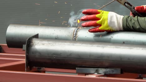 a welder works at the construction site welding pipes with an electrode, bright welding with sparks, metal, steel, blinding flashes, spot welding seams, production