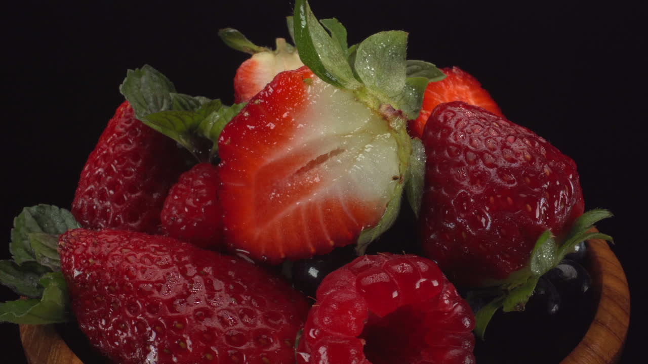 Static rotating forest berries in a wooden bowl with black background, strawberries, blueberries, raspberries, healthy fruits, 4K shot
