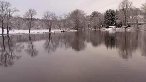 White-ice-lake-mirror-reflections-from-trees-in-water-surface-low-aerial-view