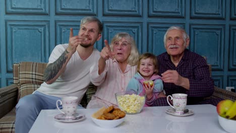 Multigenerational-family-watch-TV-with-young-girl-kid-at-home,-laughing-while-watching-cartoon-movie