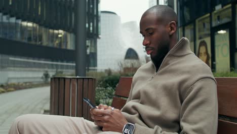 man using smartphone on a bench in the city