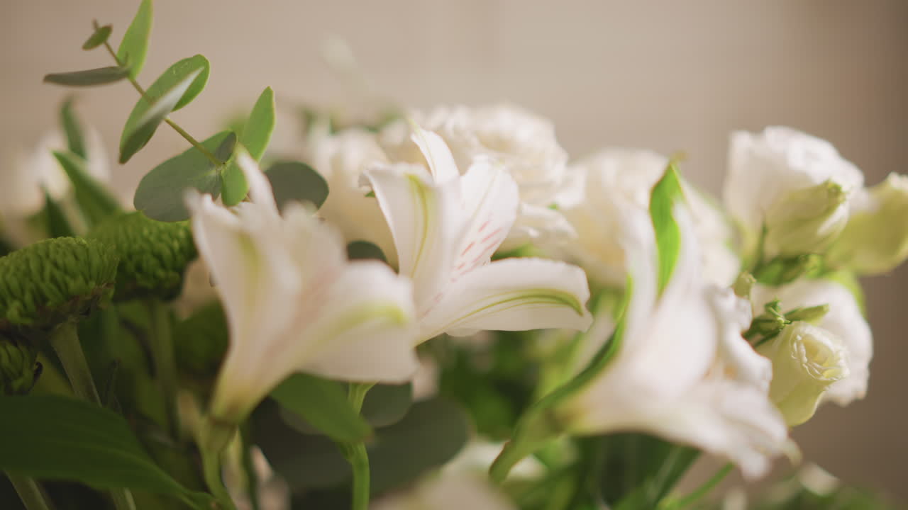 Hvid blomsterbuket på hjemmebord, blødt morgenlys, nærbillede af liljer og roser med eukalyptus og grønne krysantemum, lav dybdeskarphed, varm neutral baggrund, sarte kronblade.