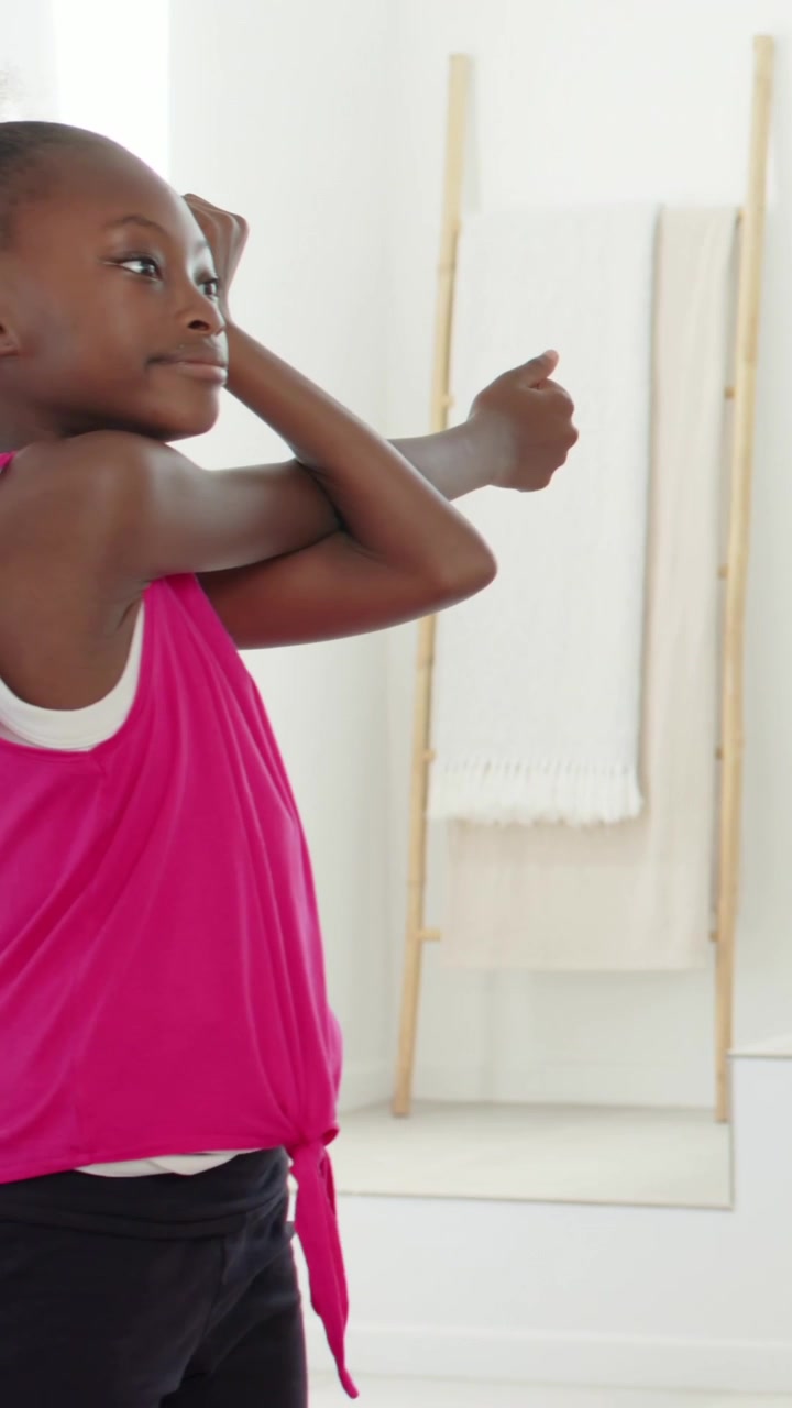 Vertical video: Stretching girl in pink top doing chest pull at home with ladder, plant, copy space