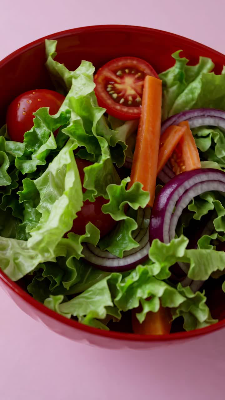 Close-up top view of a fresh salad in a red bowl, featuring lettuce, tomatoes, carrots, and onions
