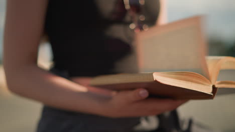 close-up of individual holding a brown book cover with fast-flipping pages to the right,sunlight illuminates the book while the background remains blurred