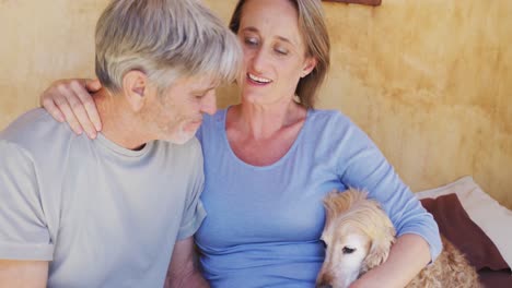 una pareja caucásica mayor sonriente abrazándose y relajándose en el porche con un perro mascota