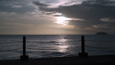 puesta de sol sobre el mar con pequeñas olas rodando hacia el terraplén y la luz del sol reflejada en el agua