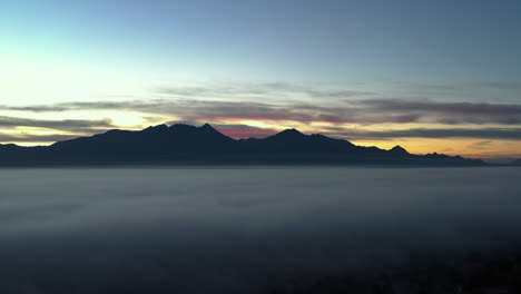 Thick-fog-over-valley-with-mountain-range-in-distance,-aerial-view