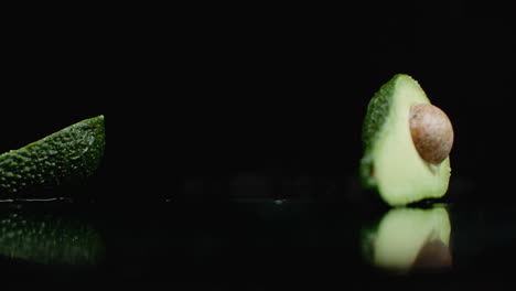 los aguacates verdes maduros están cayendo sobre el vidrio con salpicaduras de agua en cámara lenta sobre un fondo oscuro