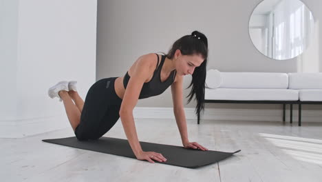 young sexy brunette woman in sportswear performs pushups kneeling at home on a rug