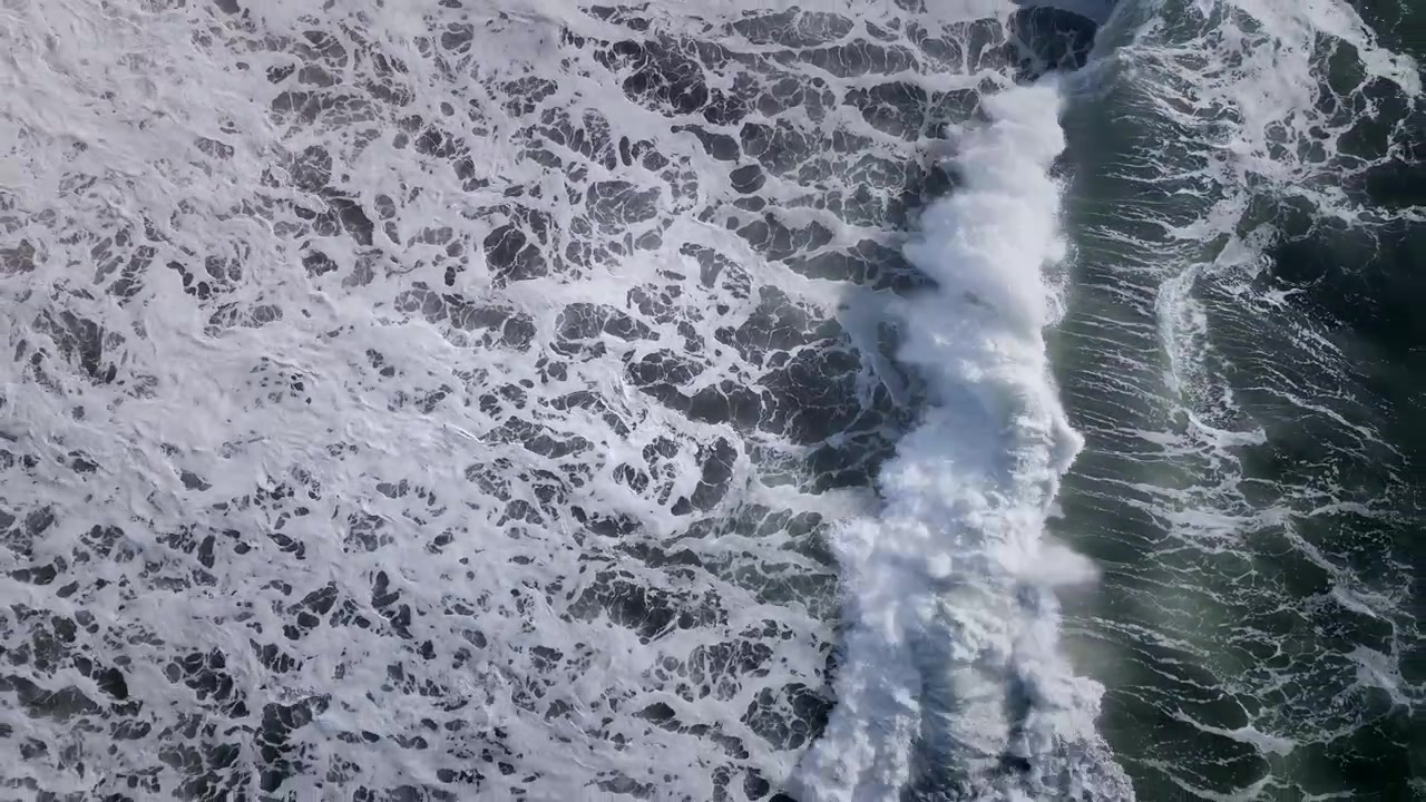 Top down aerial footage of turbulent ocean surface with white sea foam patterns and rolling waves, natural water background texture for coastal and marine themes