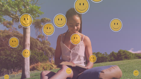 animación de iconos emoji sobre una mujer biracial sonriente leyendo en el parque