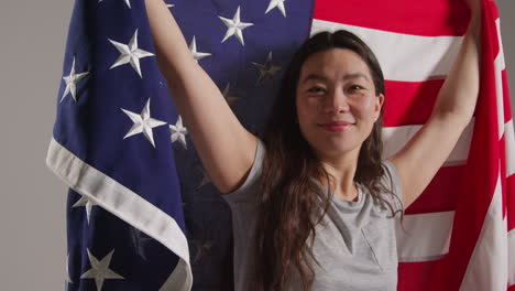 studio portrait shot of woman wrapped in american flag celebrating 4th july independence day