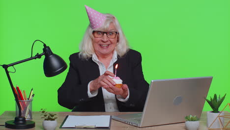 Una-Mujer-De-Negocios-Senior-Celebrando-Un-Cumpleaños-Solitario-En-La-Oficina-Soplando-Velas-En-Un-Pastel-Pequeño-Pide-Un-Deseo
