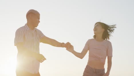 happy biracial couple dancing together at beach, in slow motion