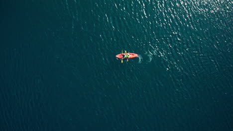 two people paddle orange kayak in wavy water, wide overhead aerial