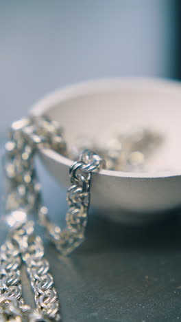 cu: man puts finished silver chain into white bowl on scale against blurred background in jewelry workshop closeup
