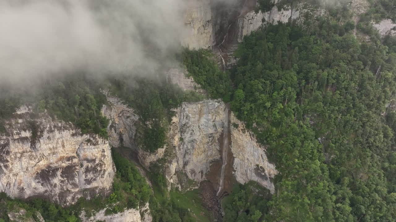 Drone rising into clouds with aerial view of Seerenbach Falls in Switzerland