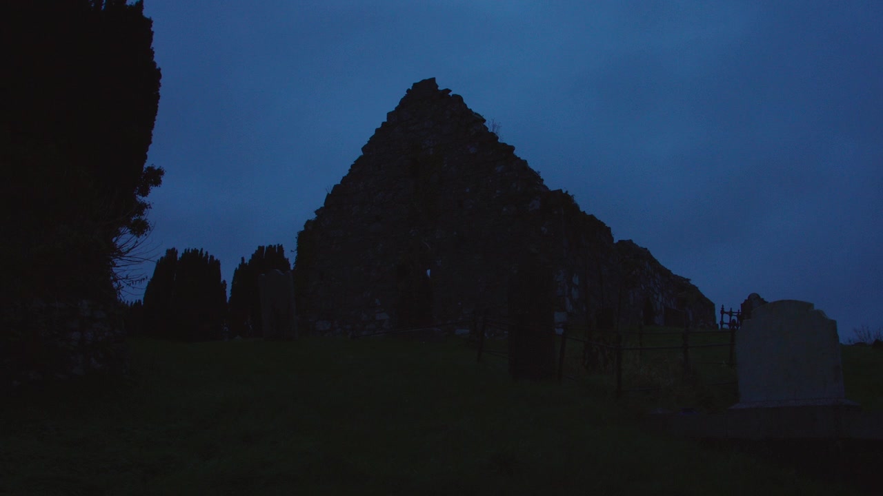 Ruína de uma antiga igreja de pedra com túmulos na Irlanda ao anoitecer.