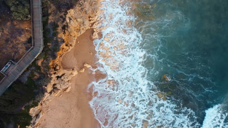 Aerial-top-down-shot-of-wooden-bridge-with-walking-people-along-rocky-coastline-of-Portugal