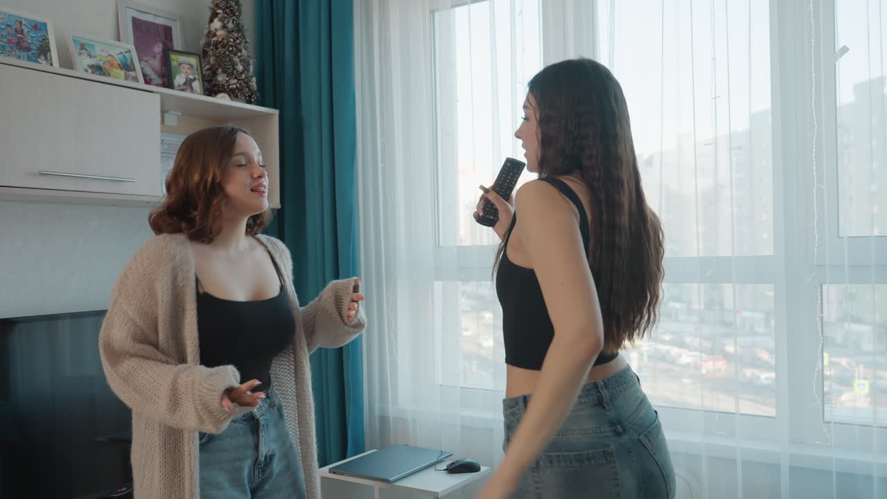 Women Duet Perform Lively Entertainment, Female Performers Enjoy Energetic Karaoke Session Near Sofa In Sunlight, Two Women Sing Together Joyfully During Lively Home Karaoke With Dancing And Laughter