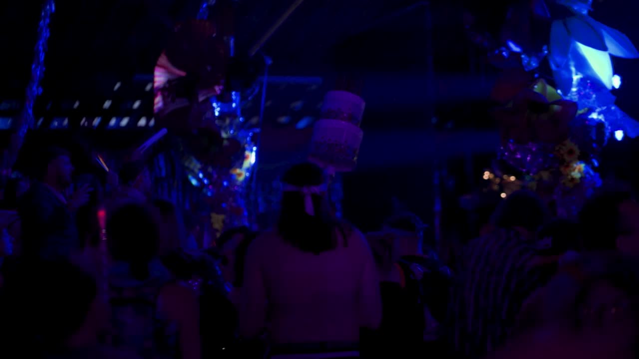 Bir gece kulübünde dans edip eğlenen insanların arkadan görünüşü.