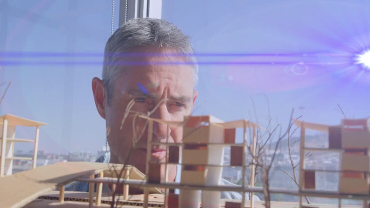 Animation of blue light beams and lens flare over male architect looking at architectural model