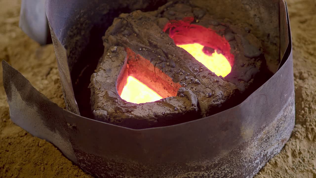Close-up shows molten alloy glowing inside a refractory mold during casting at a bell manufacturing facility, highlighting heat and artisanal technique in a traditional factory setting, slow motion