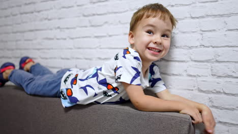 smiling caucasian baby boy lies on the sofa near the wall. cute child playing at home happily.
