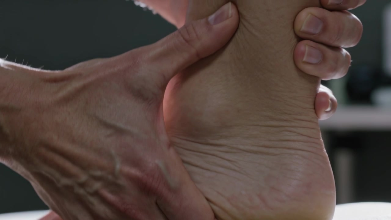 Terapista che posiziona il piede del cliente in verticale su un lettino clinico, premendo il pollice sull'arco plantare per alleviare il dolore.
