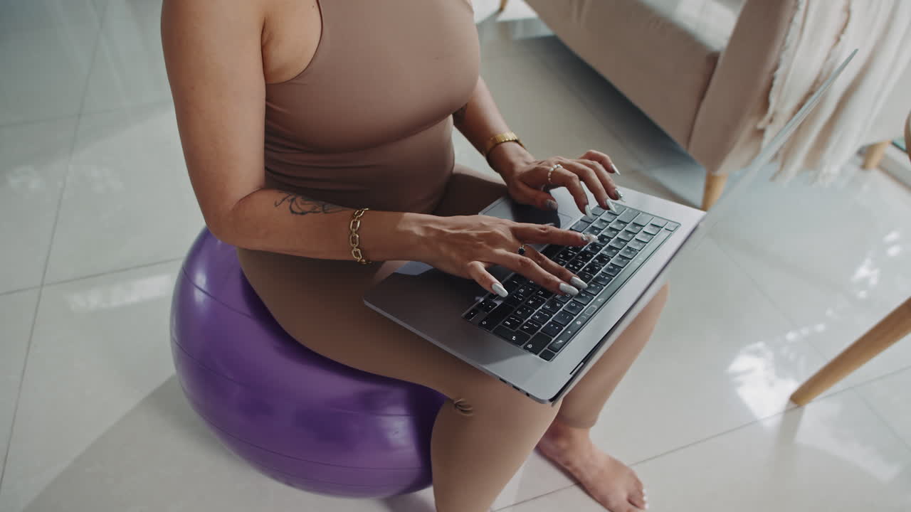 Unrecognizable Sportswoman Sitting on Fitness Ball and Typing on Laptop