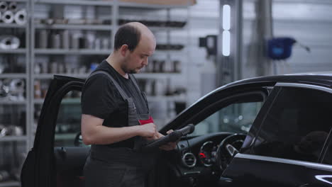 diagnósticos de automóviles. un mecánico en un servicio de automóviles de primer plano sostiene una tableta en sus manos y presiona la pantalla cerca del automóvil