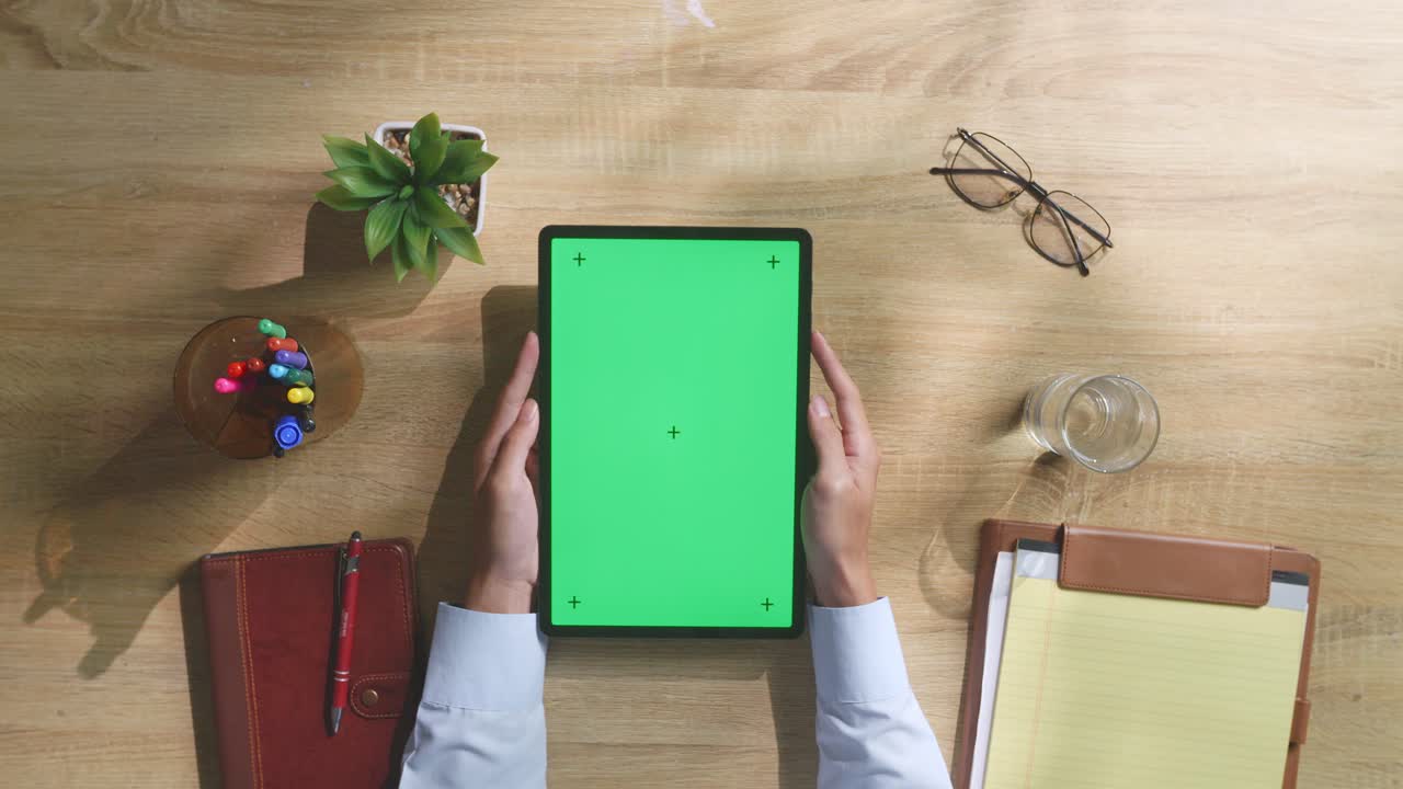vista de arriba hacia abajo de una computadora portátil con pantalla verde simulada pantalla chromakey en un escritorio de oficina de madera al lado de la libreta con bolígrafos, gafas y un vaso de agua.