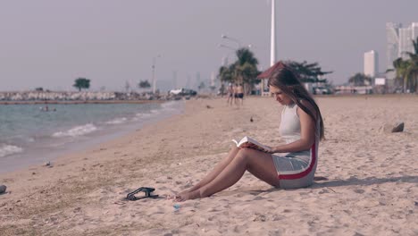hermosa dama con cabello largo y oscuro lee un libro en la playa de arena