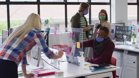 Diverse-business-people-wearing-face-masks-using-a-board-in-modern-office