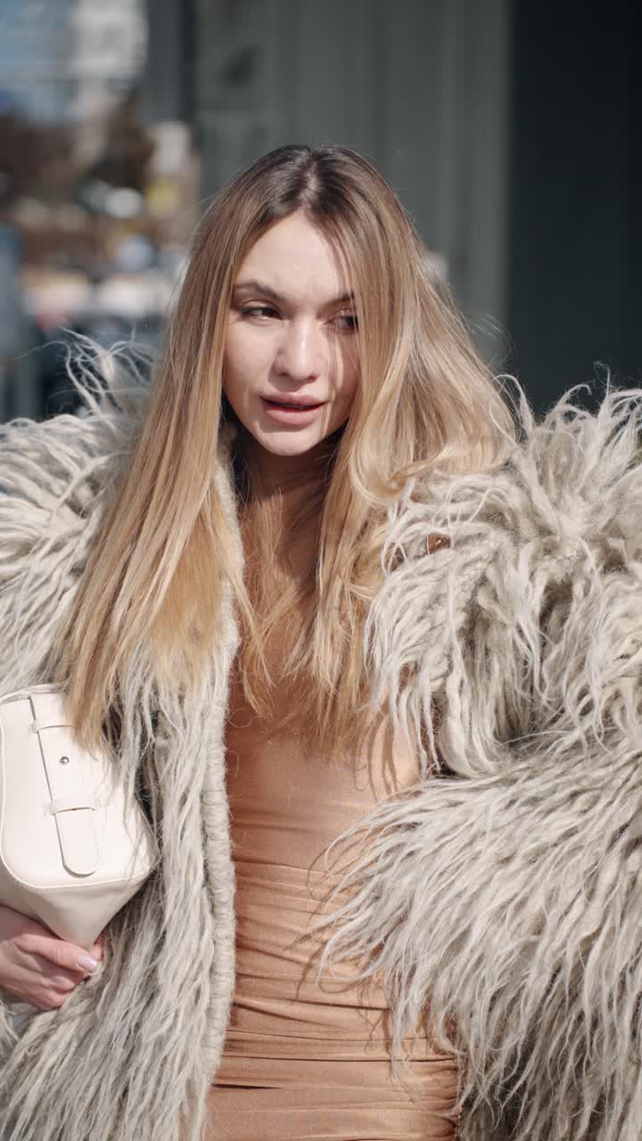 A stylish fashion influencer woman in a shaggy gray faux fur coat paired with a golden-toned clung outfit and holding a sleek white handbag, exuding a chic and trendy aesthetic posing outdoors