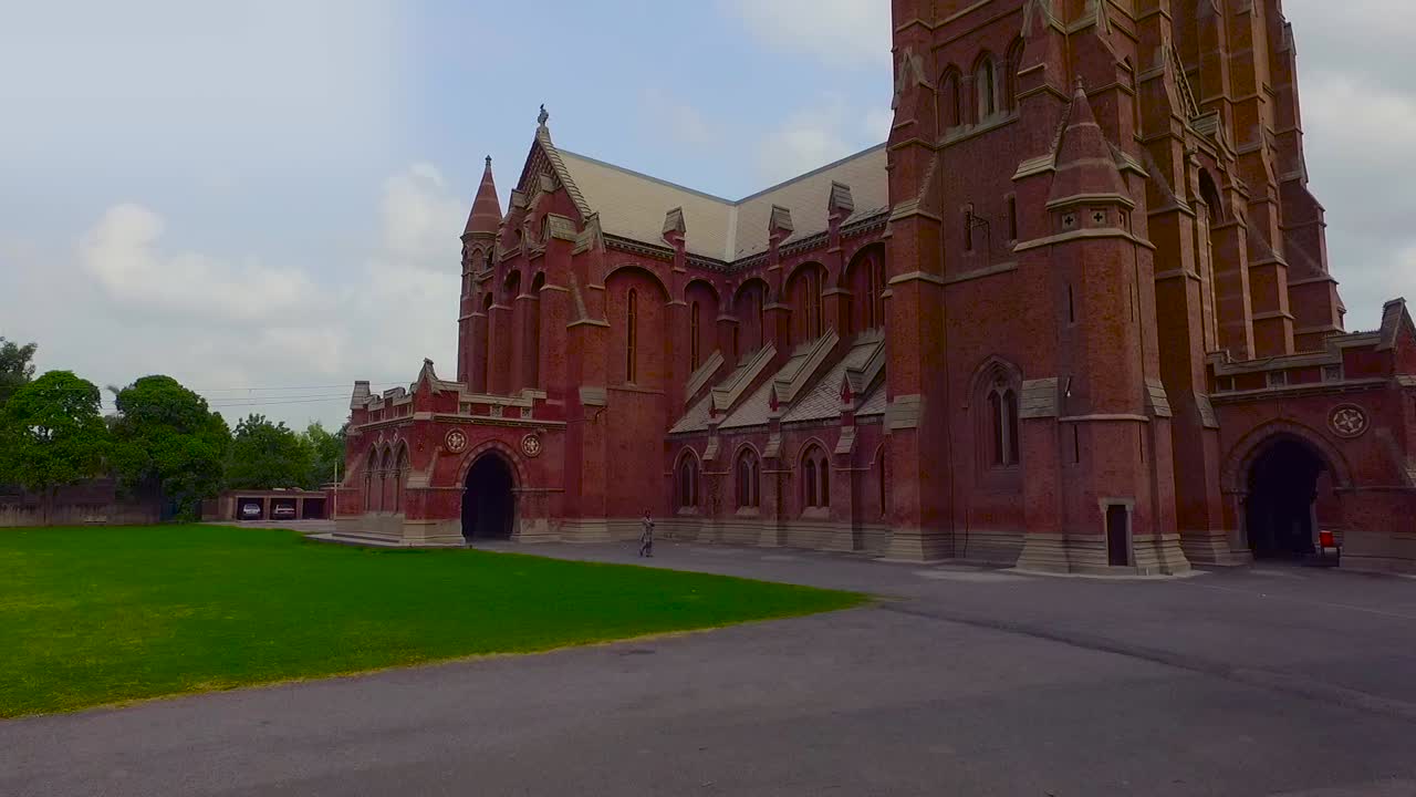 드론, 푸른 나무, 교회 주변의 잔디로 아름다운 오래된 교회의 낮은 각도 전망, 두 대의 자동차가 주차장에 주차되어 있습니다.