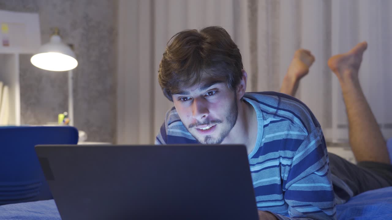 joven charlando en el portátil en la cama. feliz.