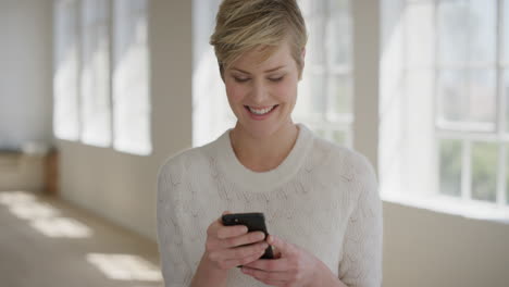 portrait of young blonde woman using smartphone enjoying texting browsing online social media messages reading sms email on mobile phone technology vibrant apartment