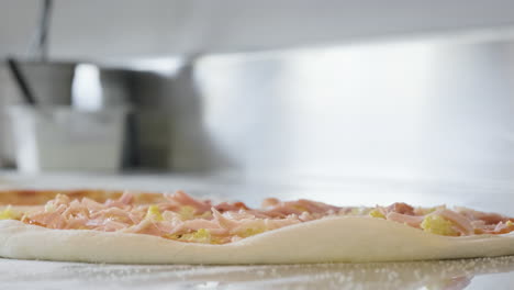 primo piano di uno chef irriconoscibile che aggiunge prosciutto sulla pasta cruda della pizza al ristorante