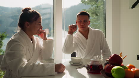 guy throws flower tea into cup sitting near lady. man creates fun moment drinking hot tea with girlfriend in morning. carefree atmosphere of couple life