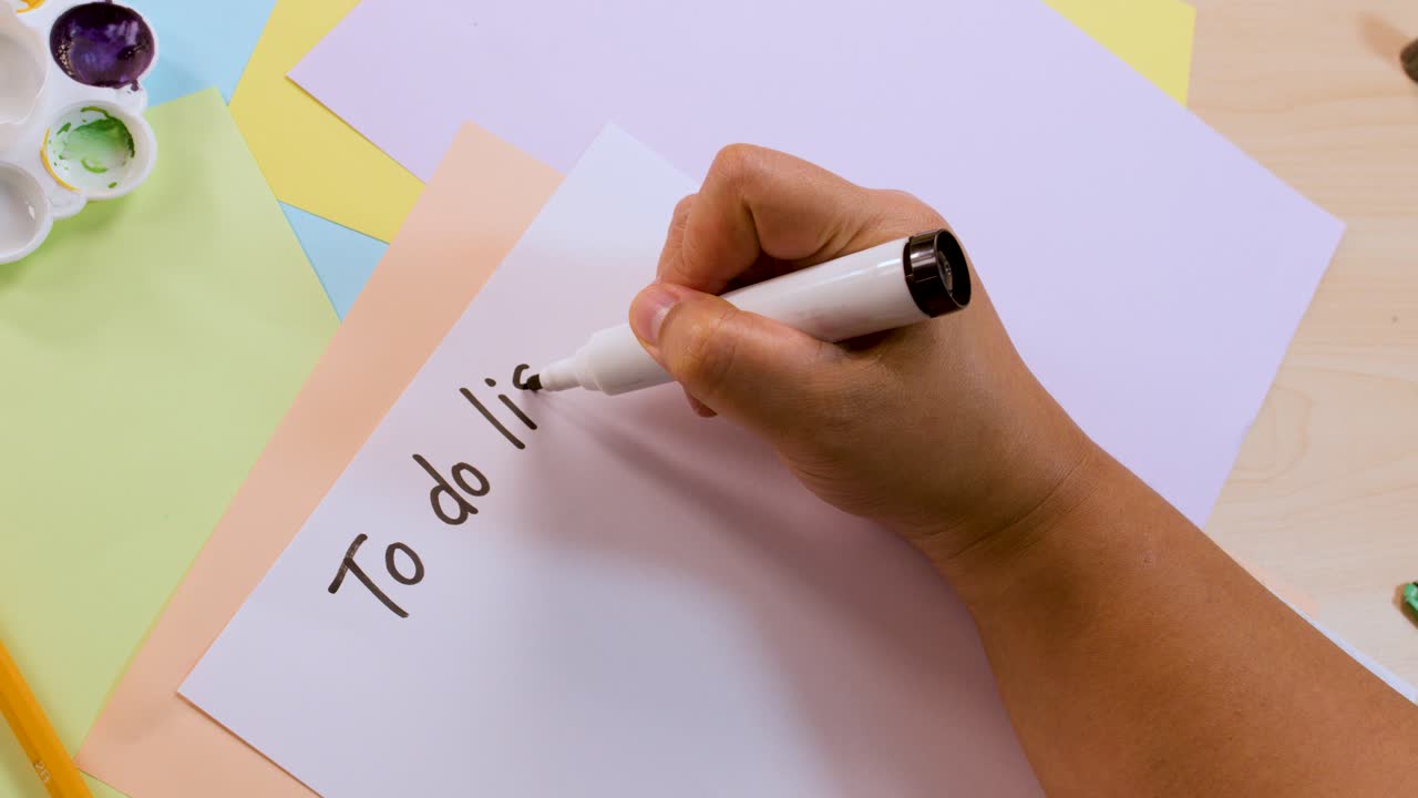 Person writes 'To do list' on paper with marker, overhead view, bright natural lighting