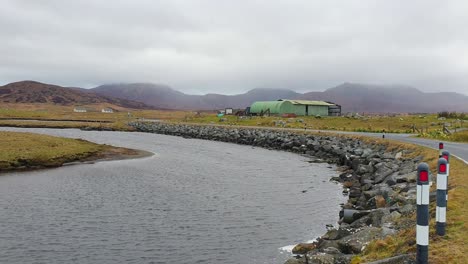 rural landscape with river, road, and mountains under cloudy sky