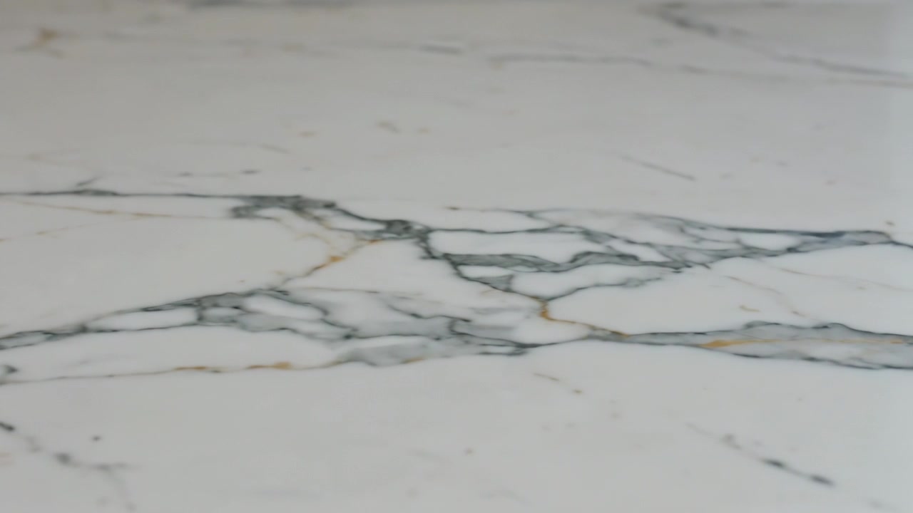 Moving camera forward right showing polished white marble slab counter showing gray gold veining