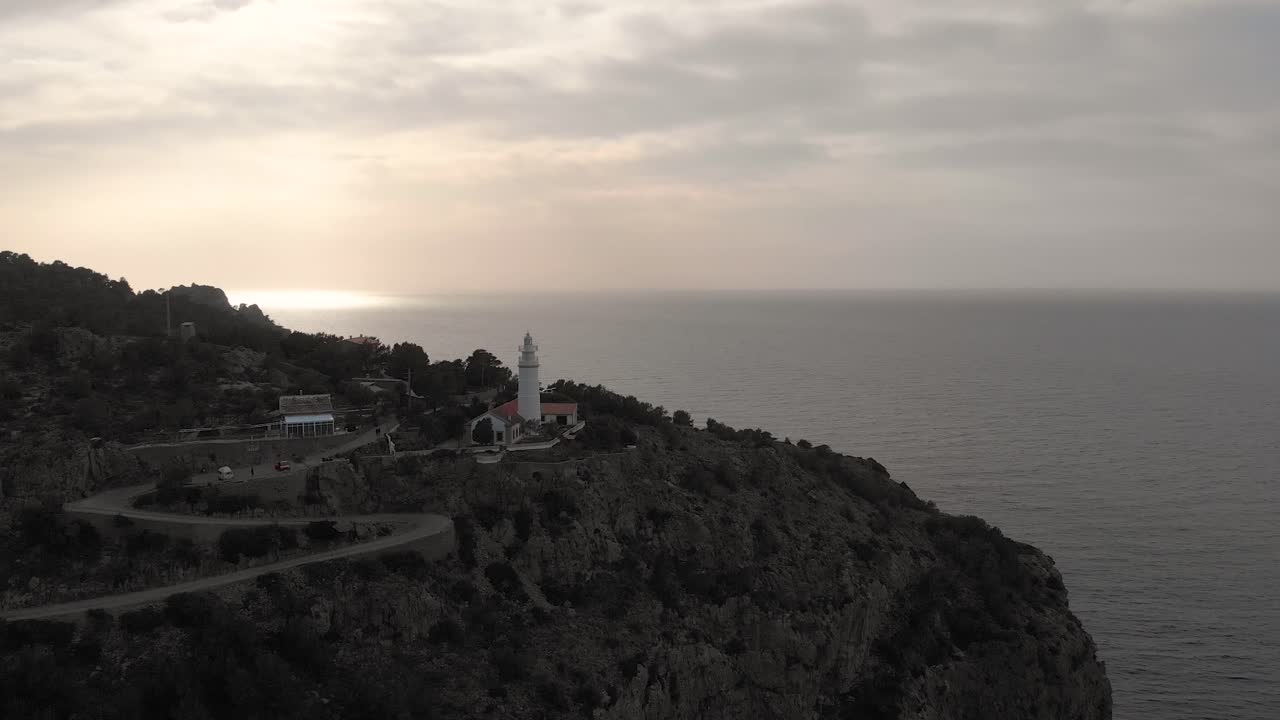 Aerial reverse, drone shot tilting away from the Far des Cap Gros lighthouse, near Soller harbor, at sunset, in Mallorca, Spain