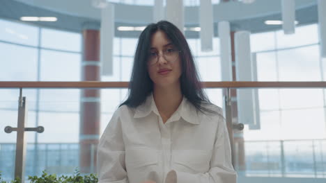 close up of young woman seated on modern bench gently closes book in her hand, surrounded by plants and contemporary glass interior, expressing calm mood and quiet focus in spacious setting