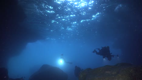 divers entering an underwater cave carrying flashlights