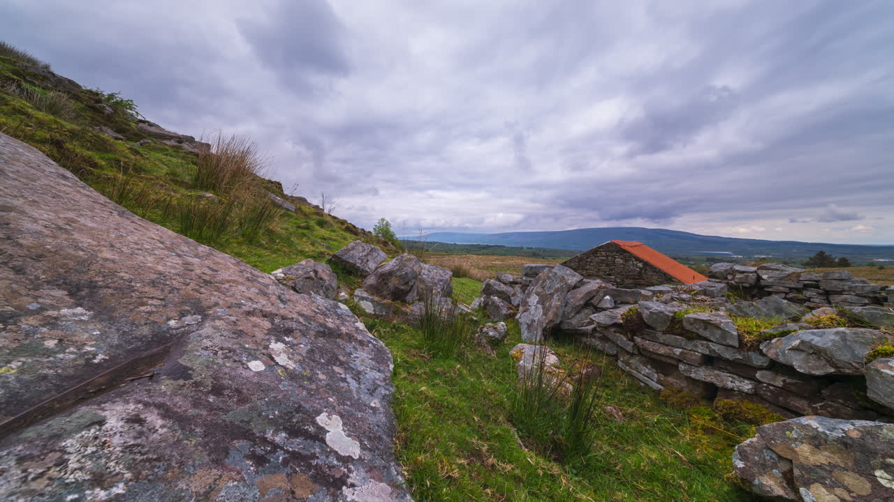 Panorama motion time lapse of rural landscape with rocky foreground and old farmhouse with hills and lake in the distance on a sunny cloudy spring day in Arigna mountains in county Leitrim in Ireland