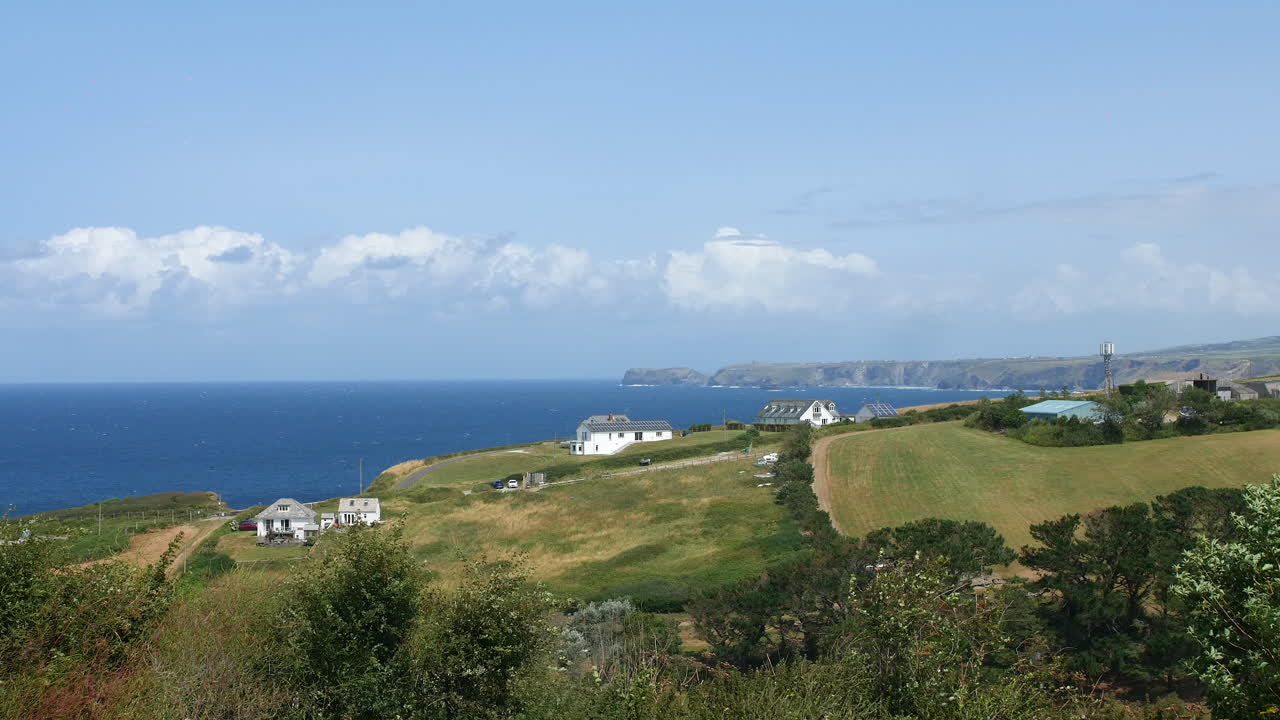 Houses scattered across rolling coastal fields overlook the ocean, with cliffs visible in the distance under a sky filled with low clouds Port Isaac, England