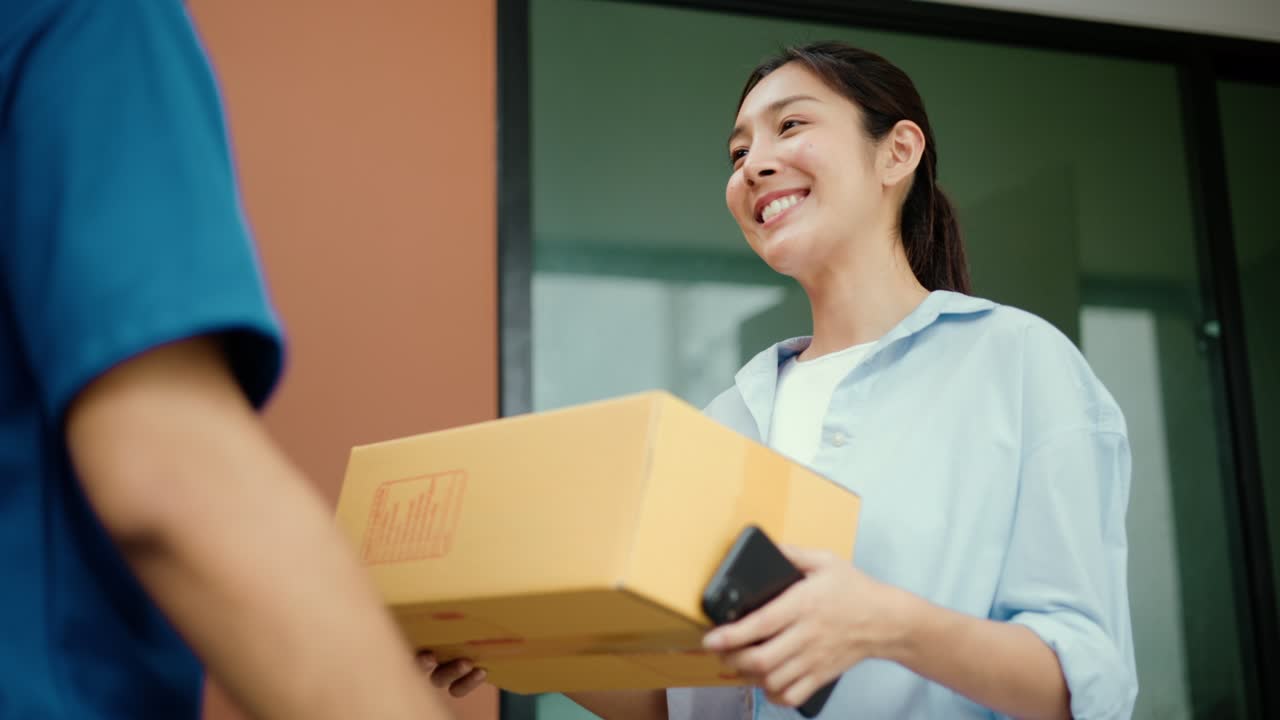 Young woman signing electronic Signature on smartphone for agreement of contract digital receiving parcel from blue delivery man from shopping online. Courier man delivering package to destination.